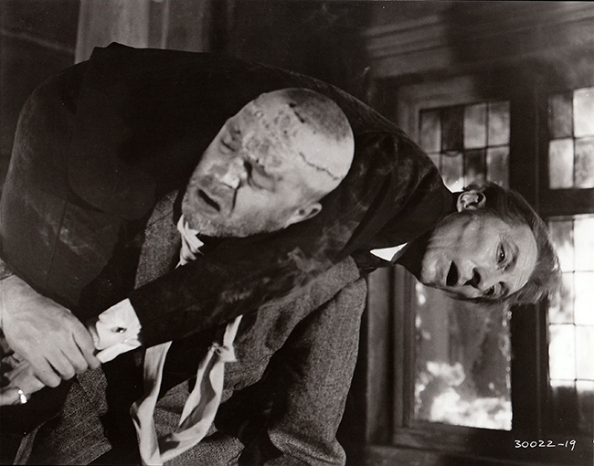 Publicity still: Freddie Jones carries Cushing back into a burning building.