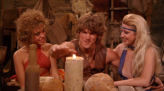 Deathstalker (John Terlesky) shows off to some tavern wenches by passing his hand through a flame. They're impressed.